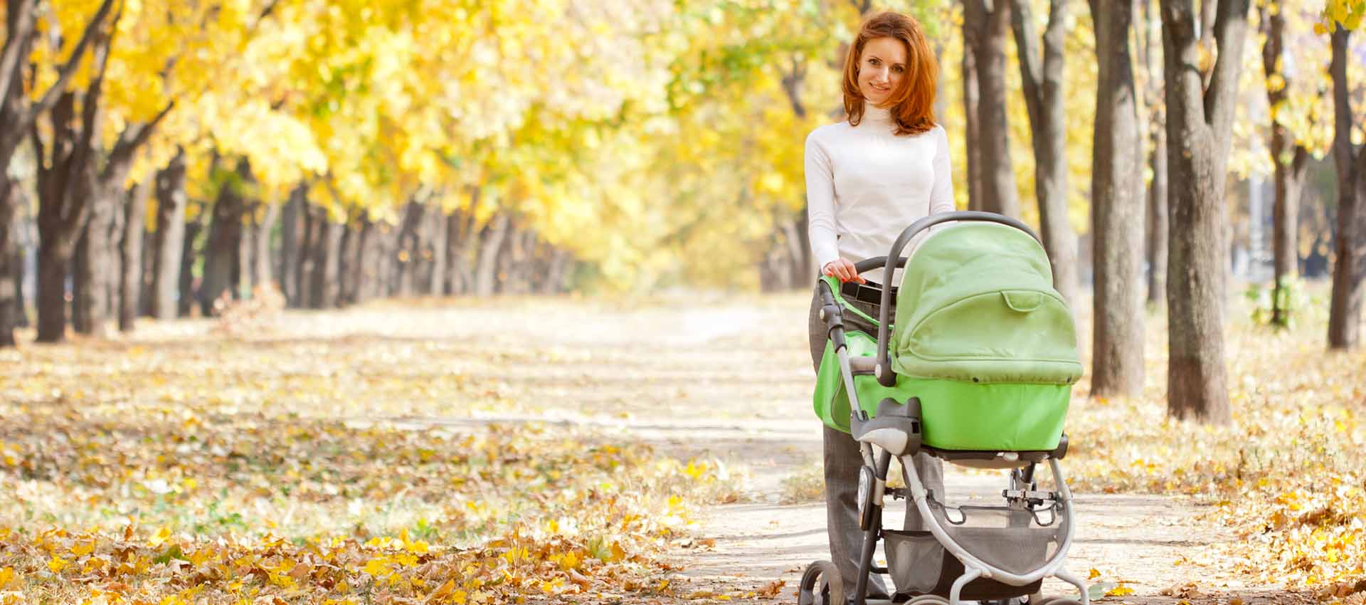 Happy young mother with baby in buggy walking in autumn park